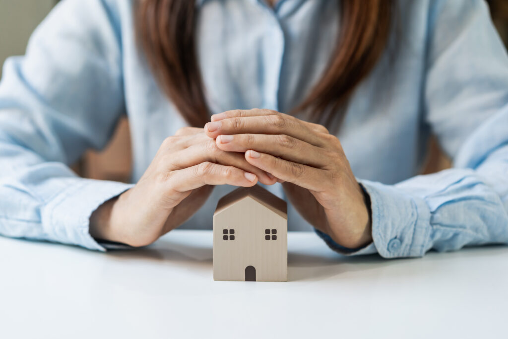 Insurance agent holding hands over small wooden house to convey home insurance.