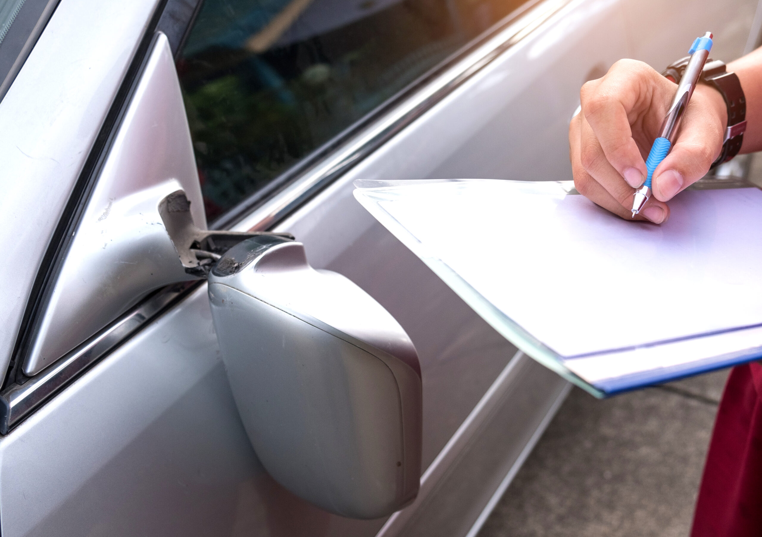 person with clipboard making note of accident damage on vehicle
