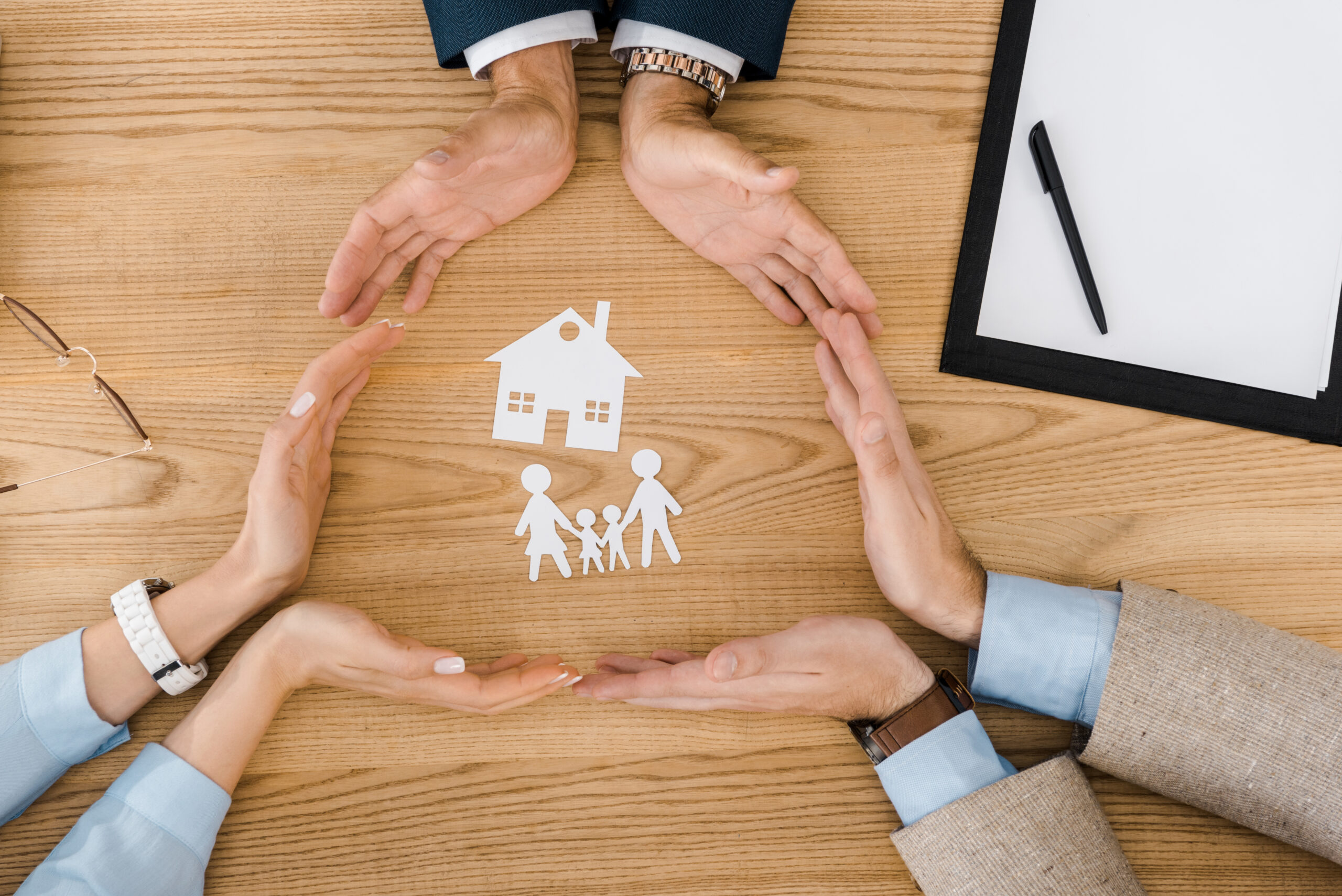 People making circle with hands on table with paper cutout of house and family in the middle