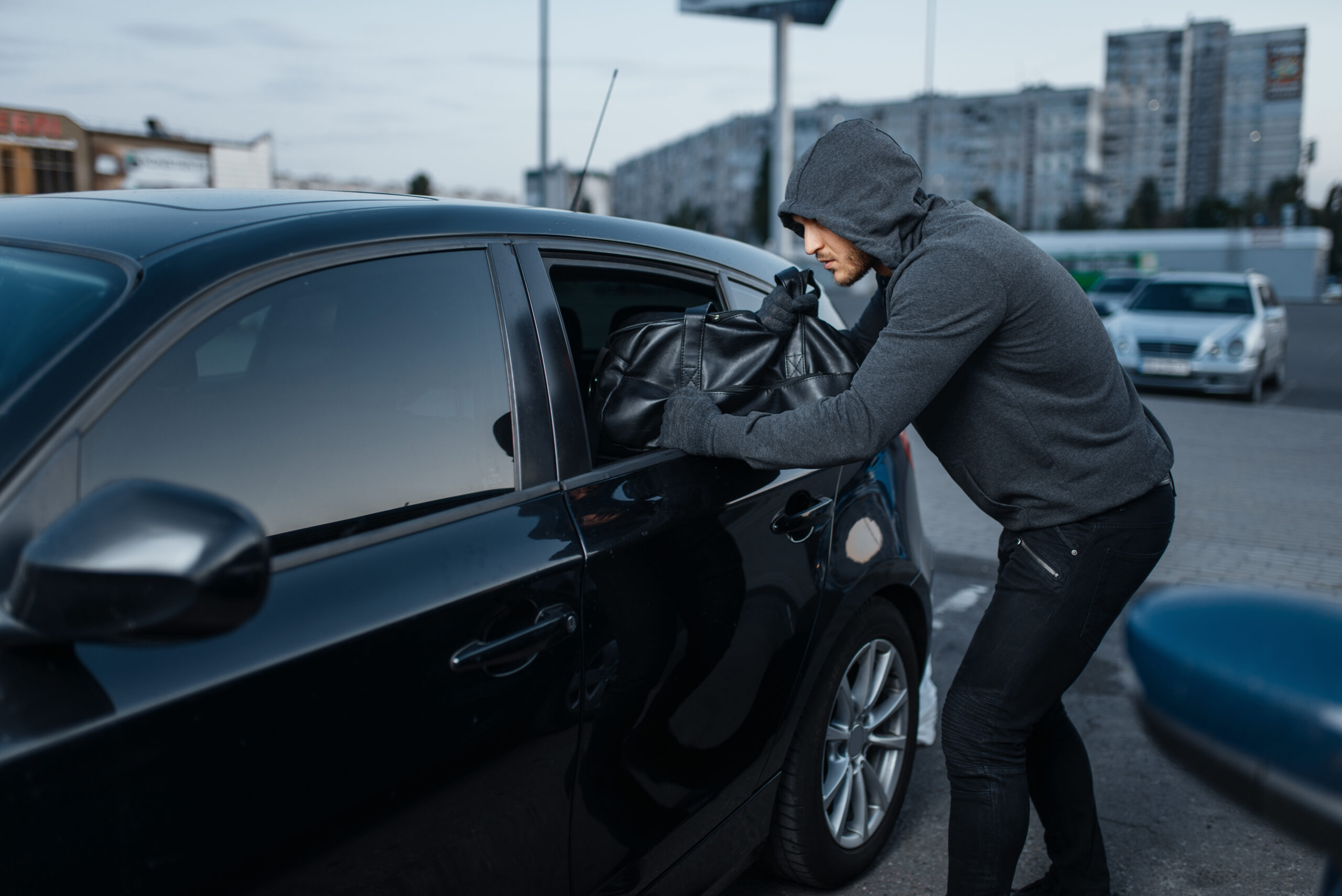 Car thief breaking door, criminal job, burglar, stealing. Hooded male robber opening vehicle on parking. Auto robbery, automobile crime