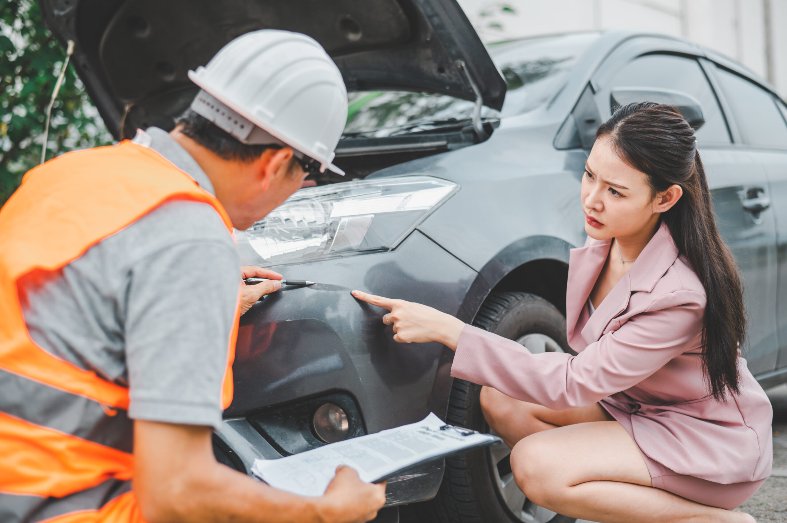 insurance adjuster inspecting damaged car with woman